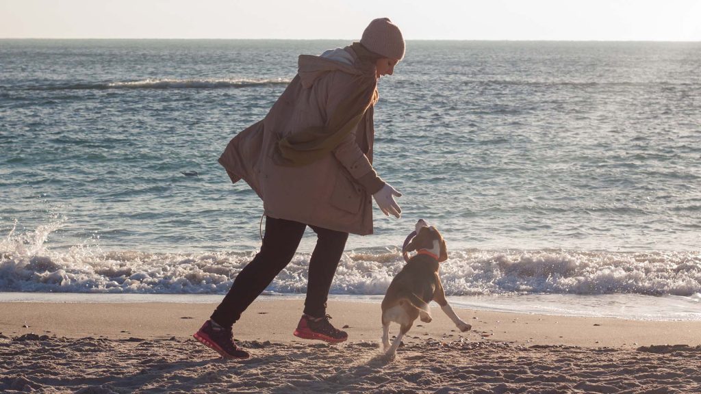 Eine junge Frau spielt mit einem Beagle am Strand